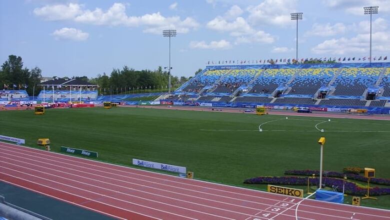 Blue and yellow stadium bleachers rise in the background with a sports field in the centre and a track in the foreground.