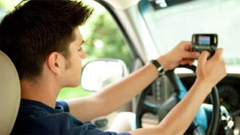 A person in the driver's seat of a car holds a phone just above the wheel.