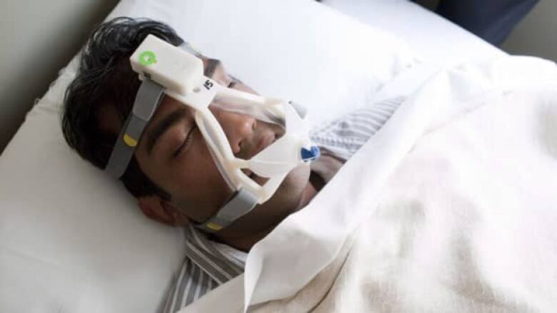 A man is pictured sleeping with an at-home sleep study test on his face.