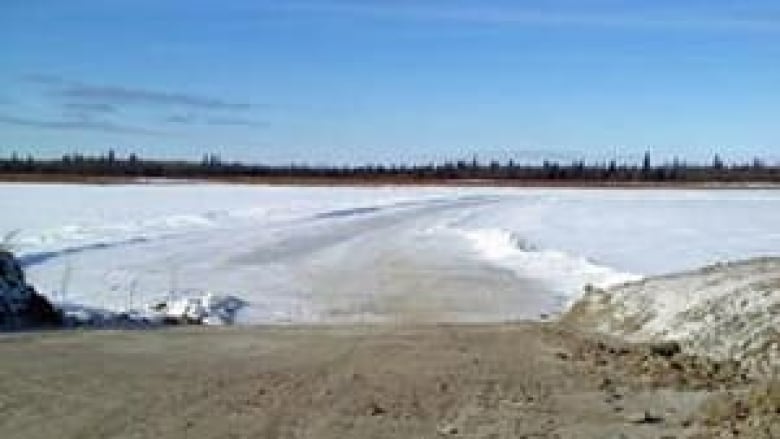 Photo of a winter road across a  lake with nothing but blue sky and a forest in the distance.