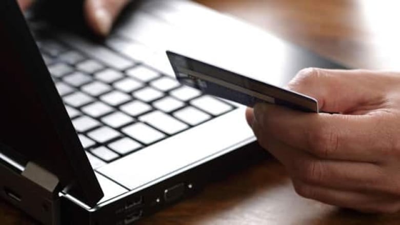 A hand is seen holding a credit card beside a laptop.