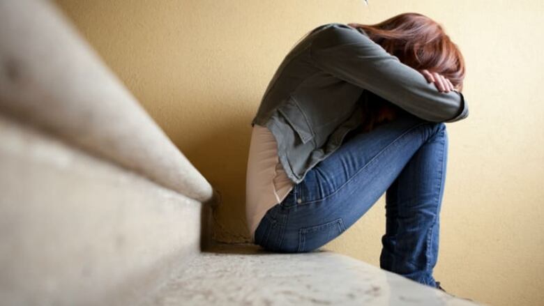 A young person sits on a staircase with her head resting on her knees.