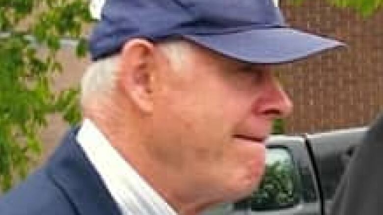 A side view of a man with white hair wearing a dark blue baseball cap.