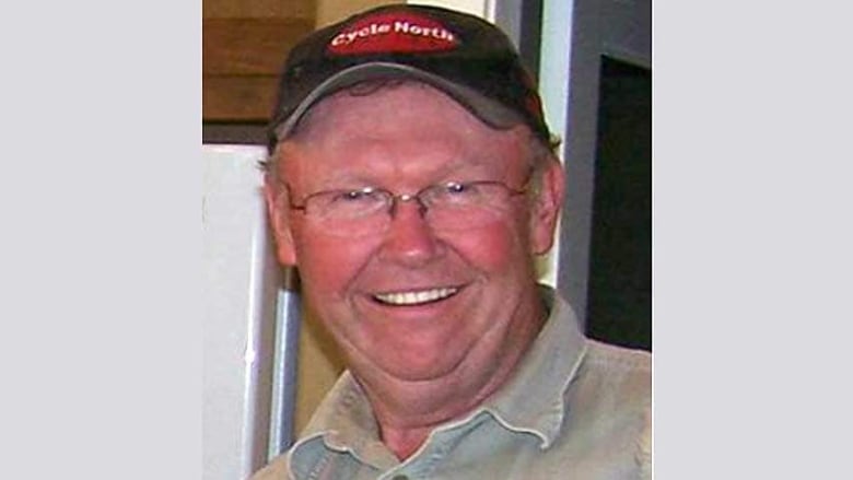 A middle aged man with a hat and glasses smiles