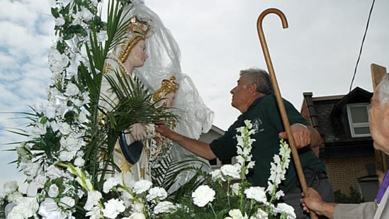 A person investigates a Virgin mary statue surrounded by flowers.