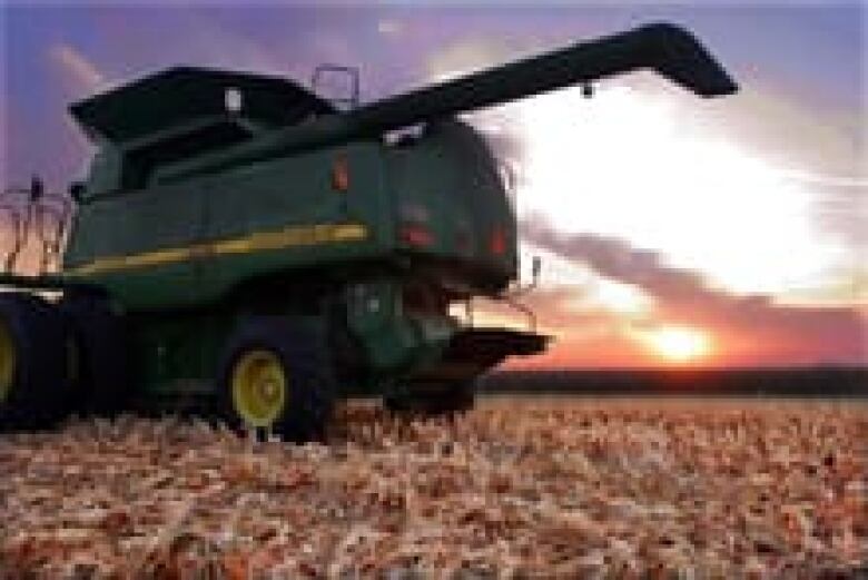 The sun rises while a John Deere combine sits idle on a freshly harvested field.