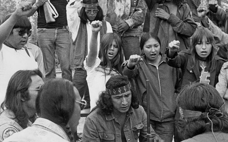 A group of people are seen holding guns and pumping their fists in the air in this black and white photo.