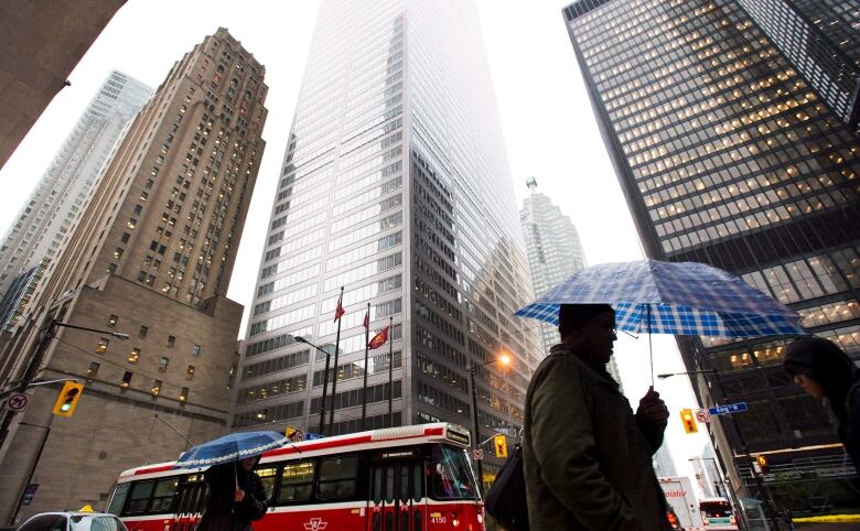 People carrying umbrellas walk past office towers.