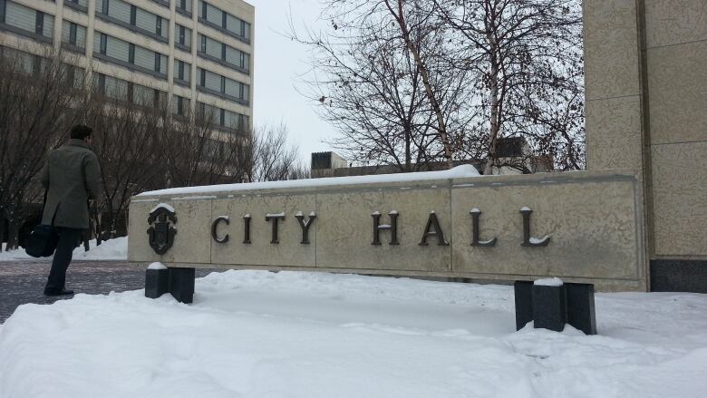 A man walks past a City Hall sign in winter