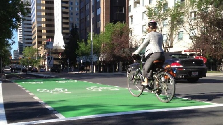 A woman on a bicycle rides in a special bike lane on a downtown street during summertime.