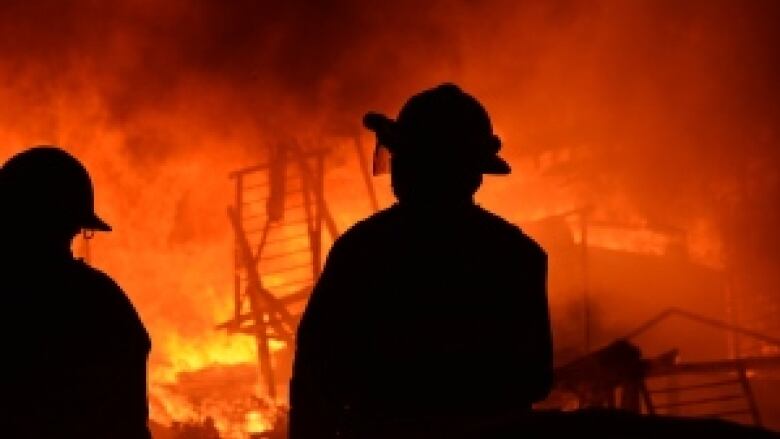 Firefighters silhouetted in front of raging inferno.