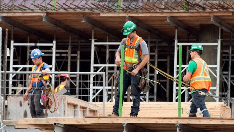 Construction workers at a building site measure out lumber.