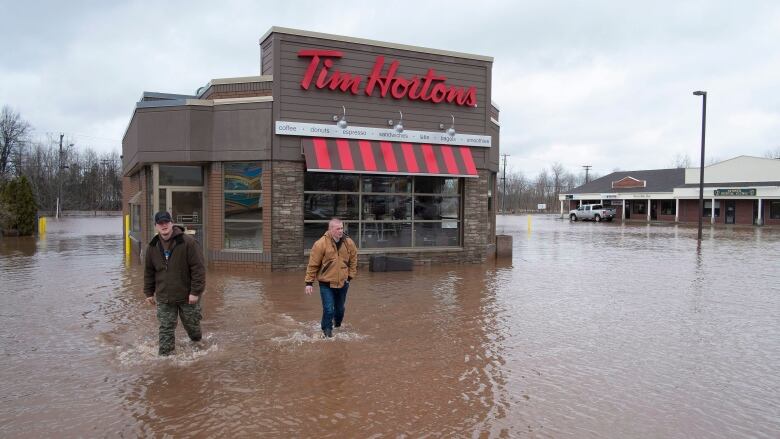 A Tim Hortons surrounded by flooding with two people walking through the water