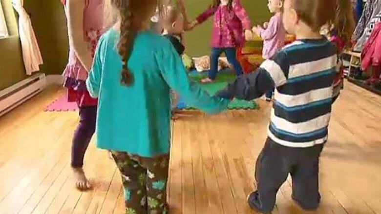 A number of young children standing in a circle, holding hands.