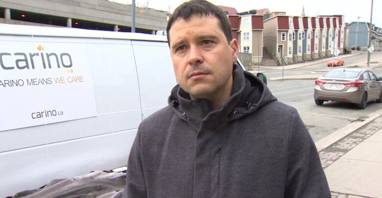 A man stands in front of a shipping van in winter.