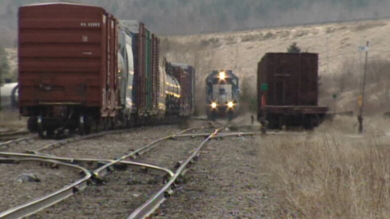 A train engine with its lights on is on train tracks with several rail cars on sidings next to it.