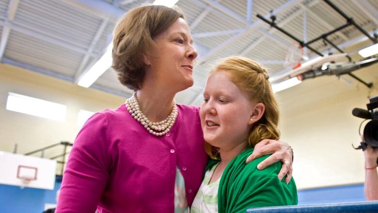 A woman hugs a girl in a basketball court. 