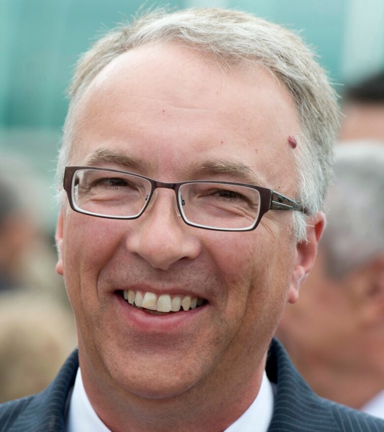 An older man in glasses smiles at the camera.