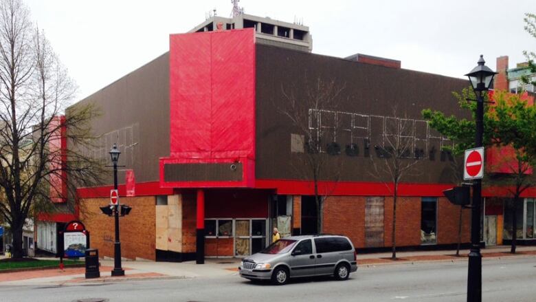 A boarded up building on a city street corner, with a vehicle driving by in the foreground.