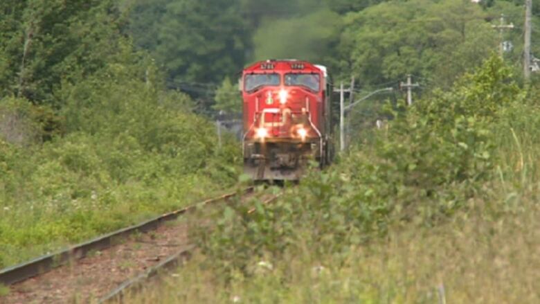 A red train engine with a white light on its front comes around a bend in the railroad tracks surrounded by green trees.