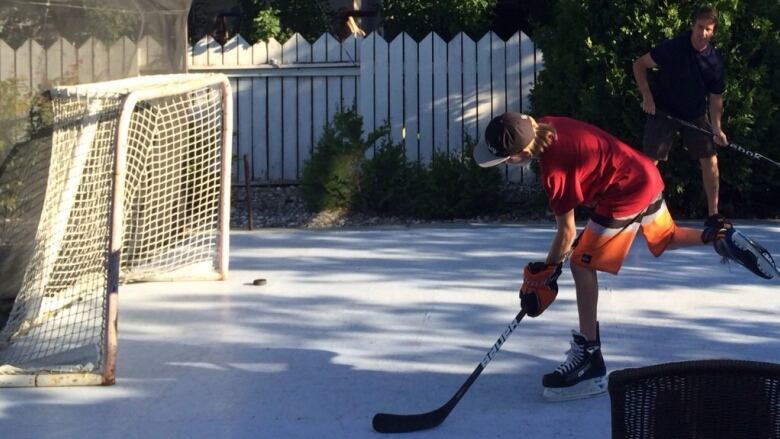 A boy wearing shorts and skates takes a shot on net with green foliage in the background