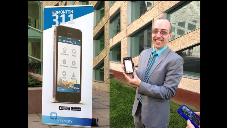 A man stands next to a sign with a smartphone.