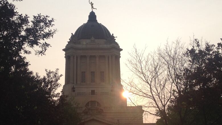 The sun rises behind the dome of a building