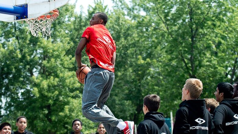 A man in a red BioSteel T-shirt goes up for a dunk at a basketball court.