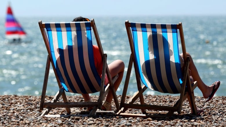 People sit on two chairs on the beach facing the water.