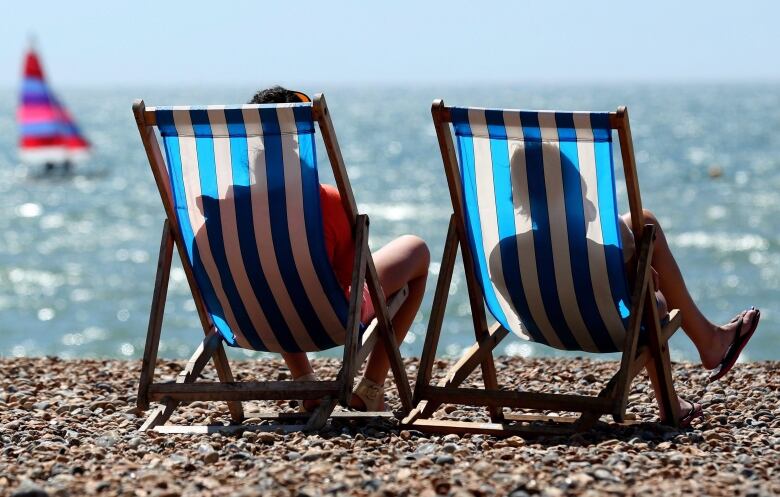 People sit on two chairs on the beach facing the water.