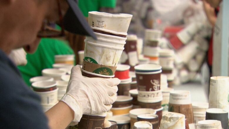 A gloved hand holds a stack of single-use coffee cups.