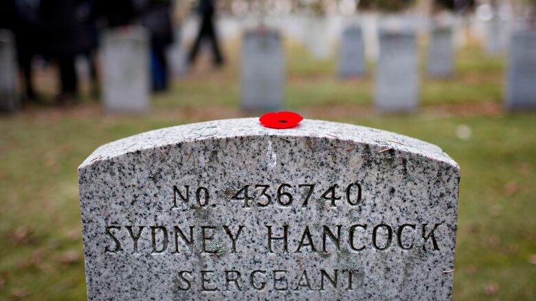 A bright red poppy sits atop a grey headstone inscribed with the words, Sergeant Sydney Hancock, 