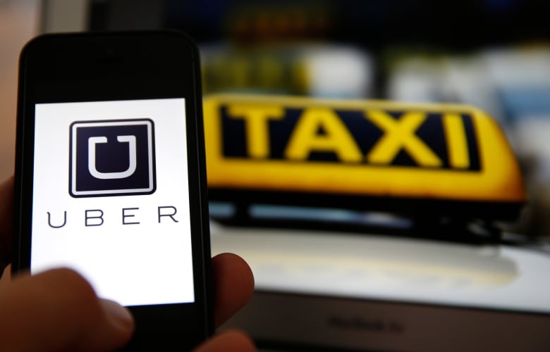 A phone with the word Uber is shown in front of yellow taxi.