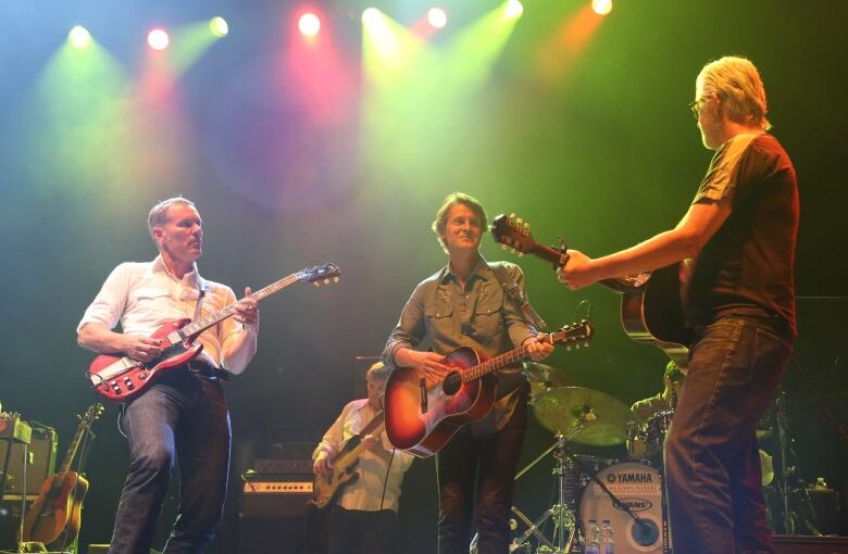 Three men play guitar on a stage. 