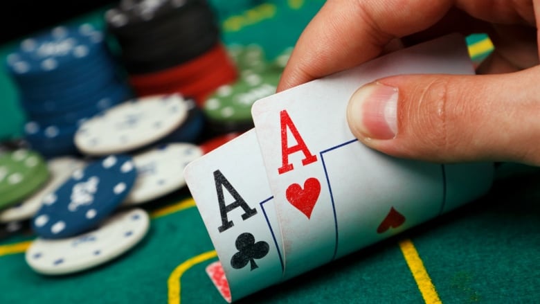 Closeup image of a hand holding an ace of clubs and ace of hearts at a poker table  