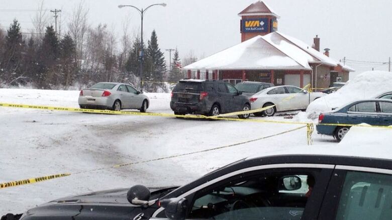 A snowy scene with multiple vehicles behind yellow police tape with a train station in the background.