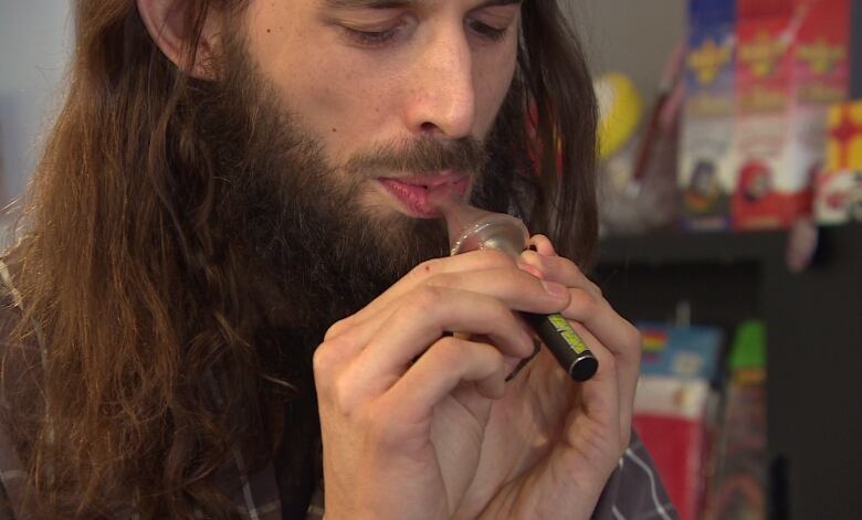 A man with long hair is shown using a vaporizer.