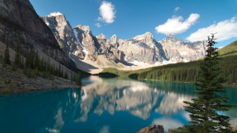 Mountains sit behind a blue lake. There are trees to the side. 