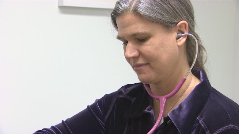 A woman with grey hair in a ponytail uses a stethoscope. 