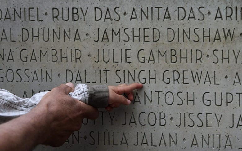 An adult hold's a child's hand as they point to one out of many names carved into a stone memorial of the victims of the Air India bombing in 1985.