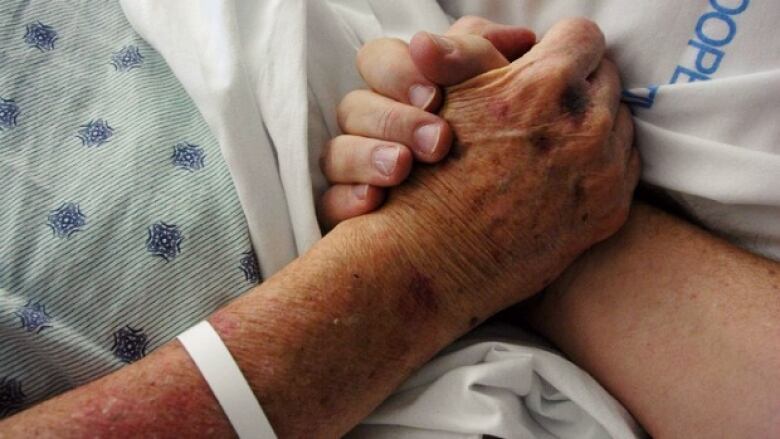 A close-up of two people holding hands - one person being a patient in a hospital bed. 