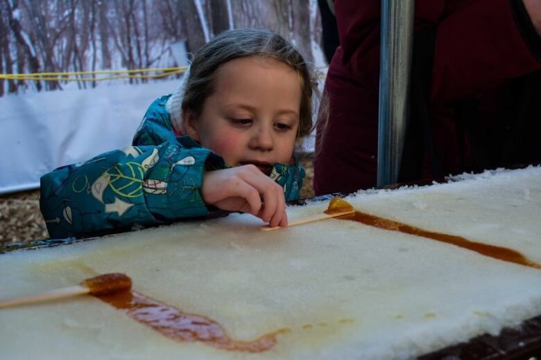 A girl holds a stick placed on a stream of maple syrup in snow on a countertop.