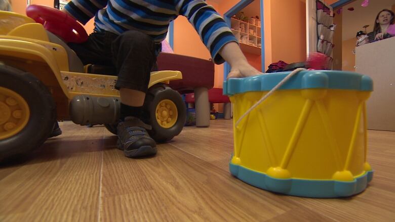 Child on a toy reaching for a drum.