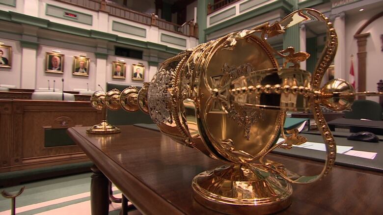 A golden House of Assembly mace sits on a wooden table.