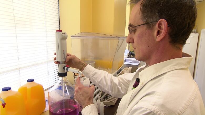 A man in a lab coat fills small bottles from a larger one.