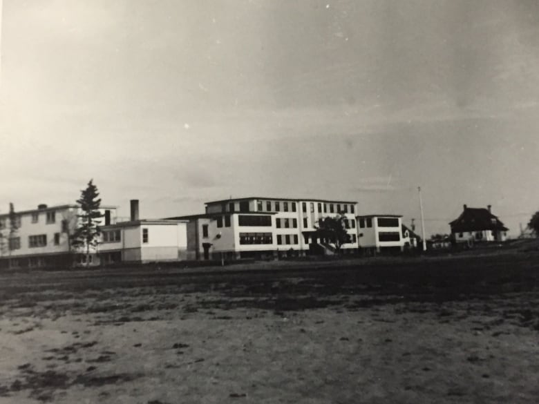 A black and white photo depicts a residential facility on a stretch of grass.