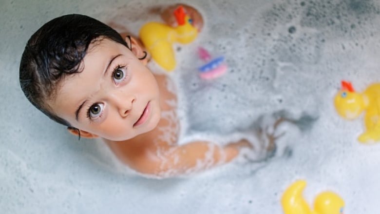 A child looks up from a bathtub with rubber duckies.