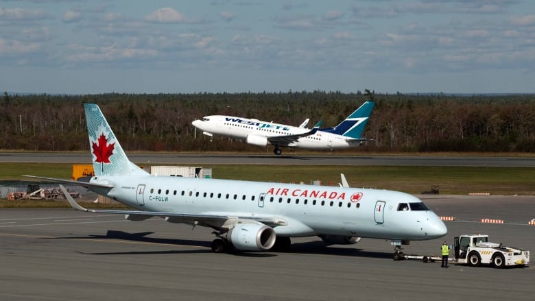 A WestJet plane takes off while an Air Canada flight taxis on a tarmac at an airport.