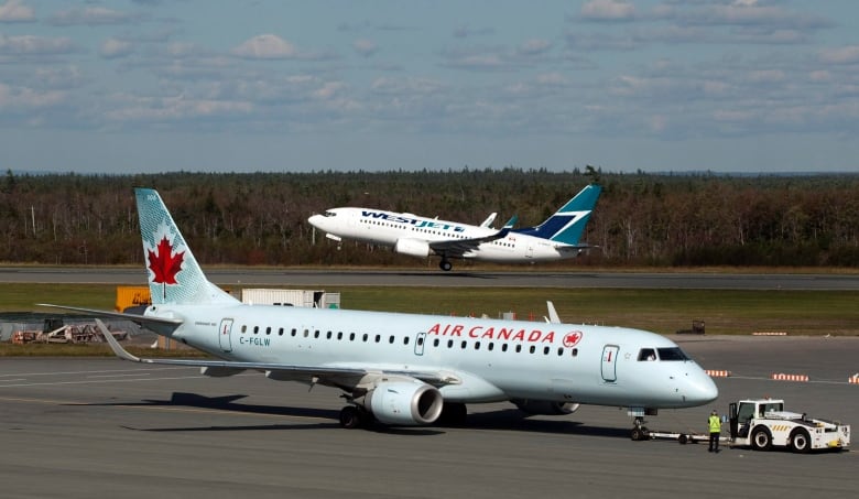 A WestJet plane takes off while an Air Canada flight taxis on a tarmac at an airport.