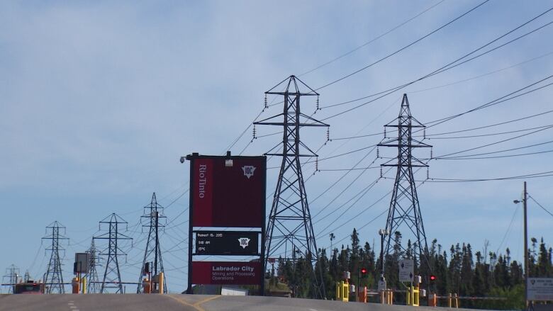 A sign for the Iron Ore Company of Canada stands tall in front of several power lines.